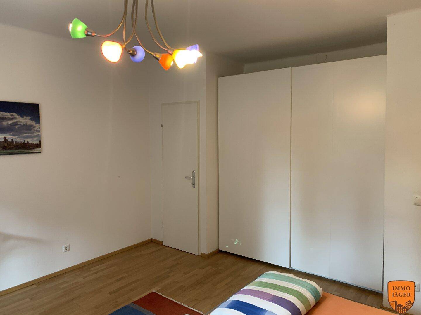 Schlafzimmer mit großem weißen Kleiderschrank und farbenfroher Deckenleuchte.