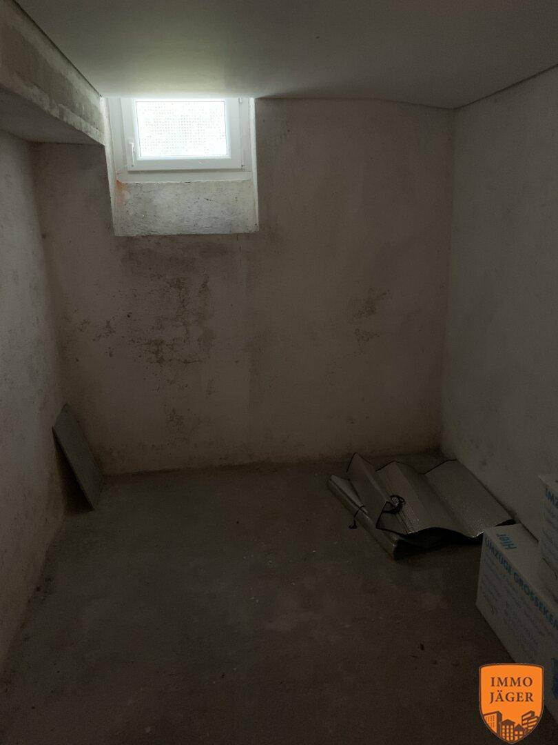Unfertiger Kellerraum mit kleinem Fenster und Betonwänden, ideal als Abstellraum.
