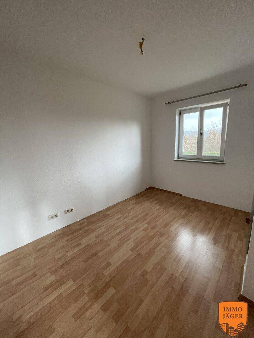 Leeres Schlafzimmer mit Laminatboden und einem Fenster, das viel Tageslicht hereinlässt.