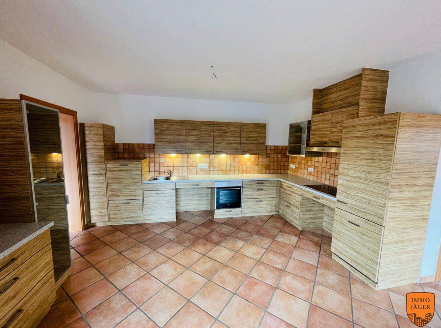 Geräumige Küche mit Holzoptik-Schränken, Terrakotta-Fliesenboden und integrierten Geräten.
