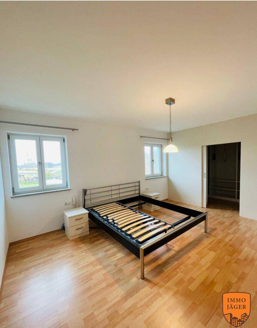 Schlafzimmer mit Laminatboden, Fenster und einem Bettgestell, bereit zur Einrichtung.
