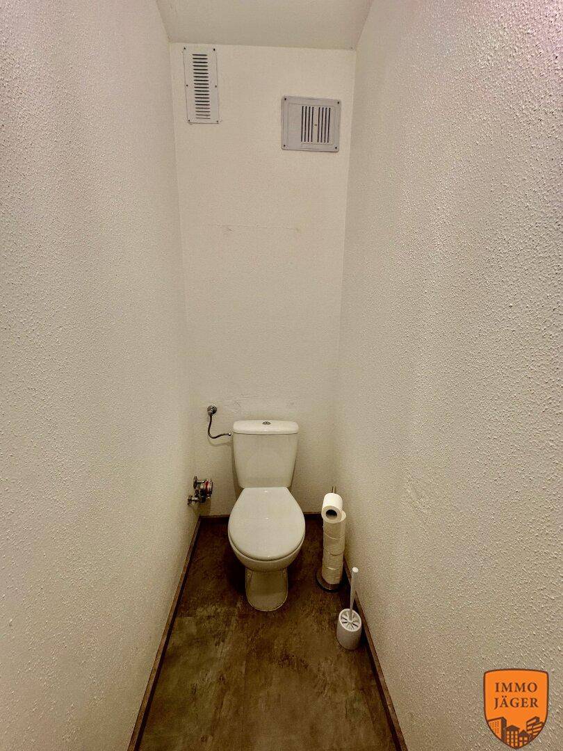 Separates WC mit Toilette und Lüftungsgittern, einfach und funktional gestaltet.