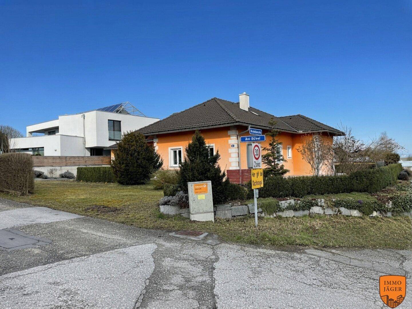 Einfamilienhaus mit orangefarbener Fassade und gepflegter Hecke in ländlicher Umgebung.