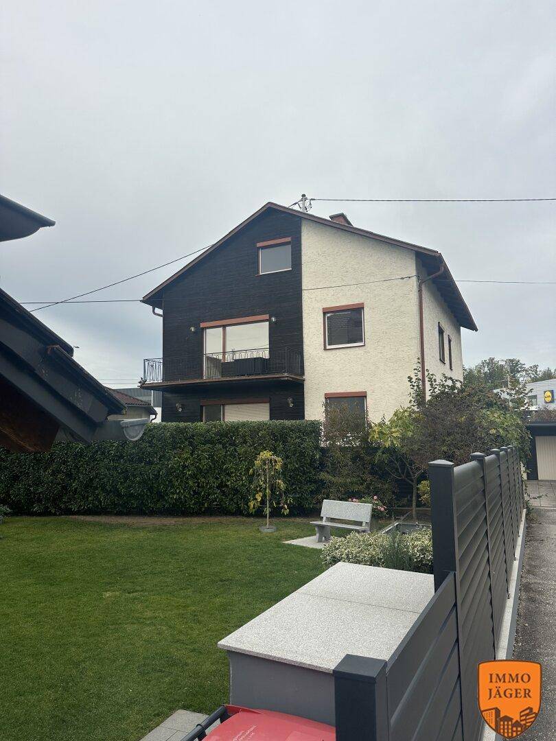 Ansicht des Hauses mit zweifarbiger Fassade, umgeben von einem gepflegten Rasen und Hecken.