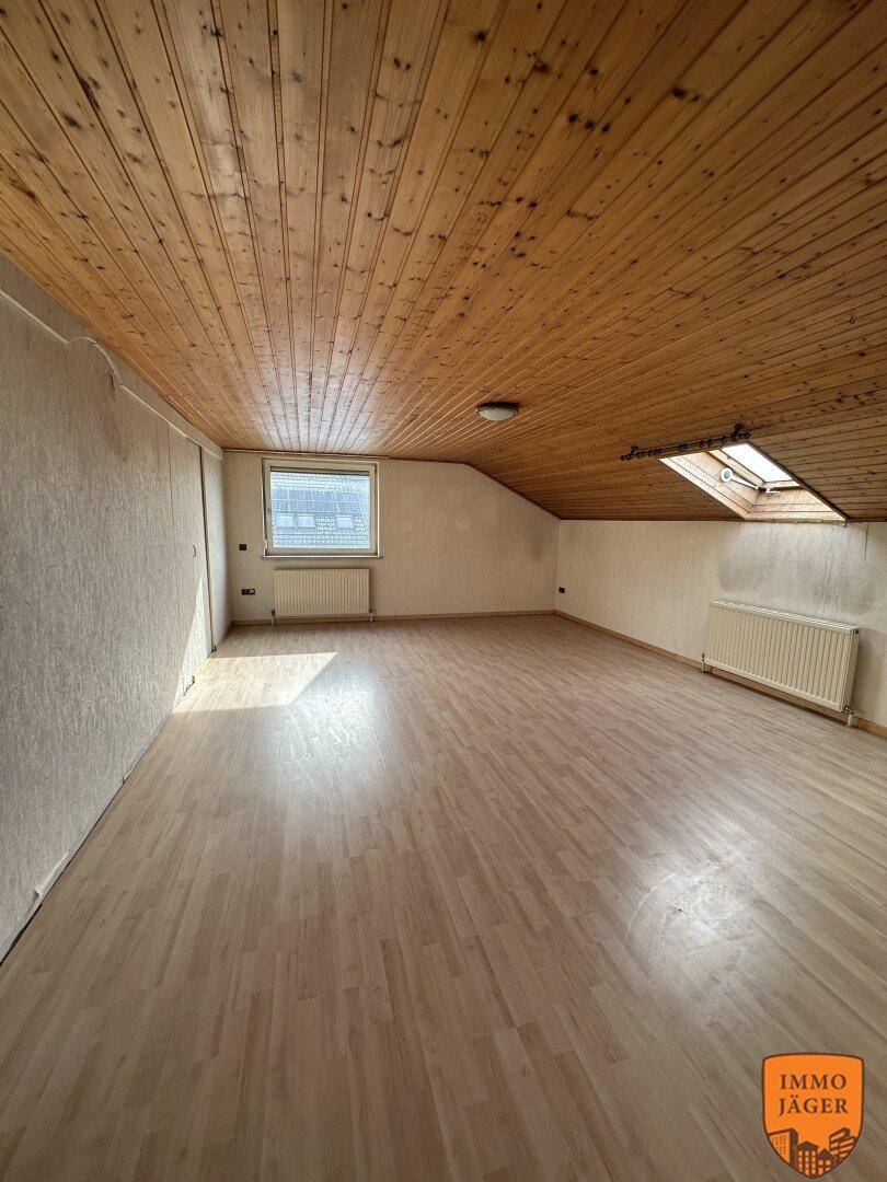 Geräumiger Dachbodenraum mit Holzvertäfelung an der Decke, Parkettboden und einem Dachfenster.