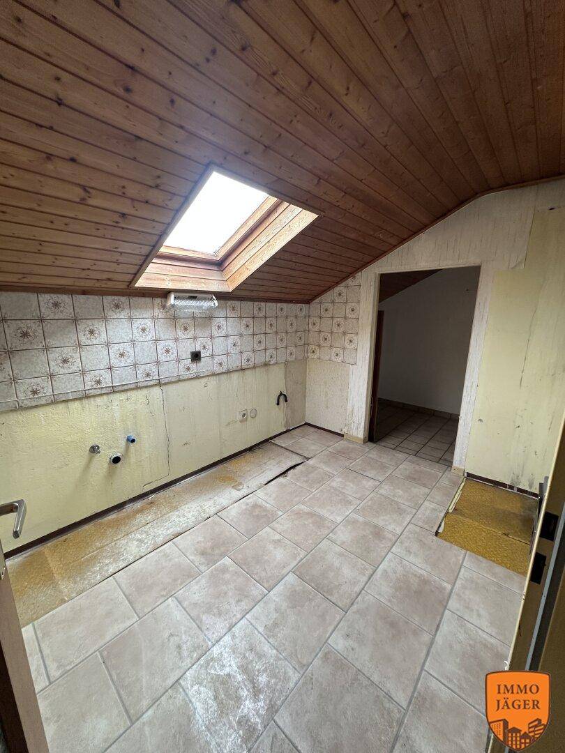 Leere Küche im Dachgeschoss mit Fliesenboden, Holzdecke und einem Dachfenster, bereit zur Renovierung.