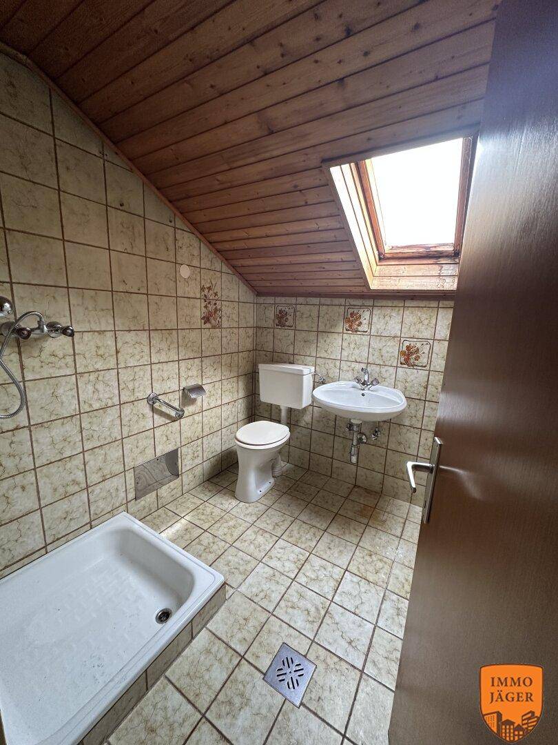 Dachgeschoss-Badezimmer mit Fliesenboden, Holzdecke, Dusche, WC und einem Dachfenster für Tageslicht.