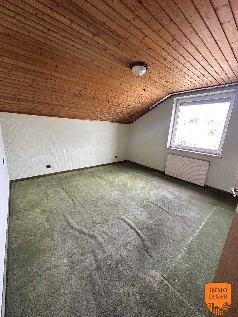 Schlafzimmer im Dachgeschoss mit grünem Teppichboden, Holzdecke und einem Fenster mit Ausblick.