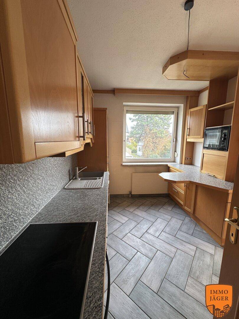 Funktionale Küche mit Holzschränken, Granitarbeitsplatte und Induktionskochfeld, gut beleuchtet.