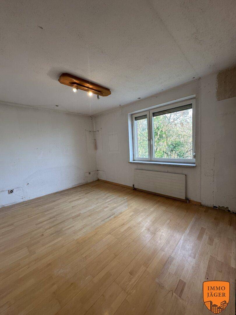 Helles Schlafzimmer mit Parkettboden und einem großen Fenster, das einen Blick ins Grüne bietet.