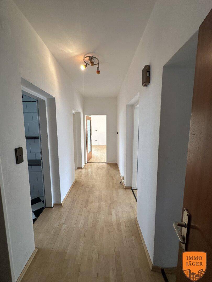 Langer, heller Flur mit Parkettboden, der zu weiteren Räumen und einem Badezimmer führt.