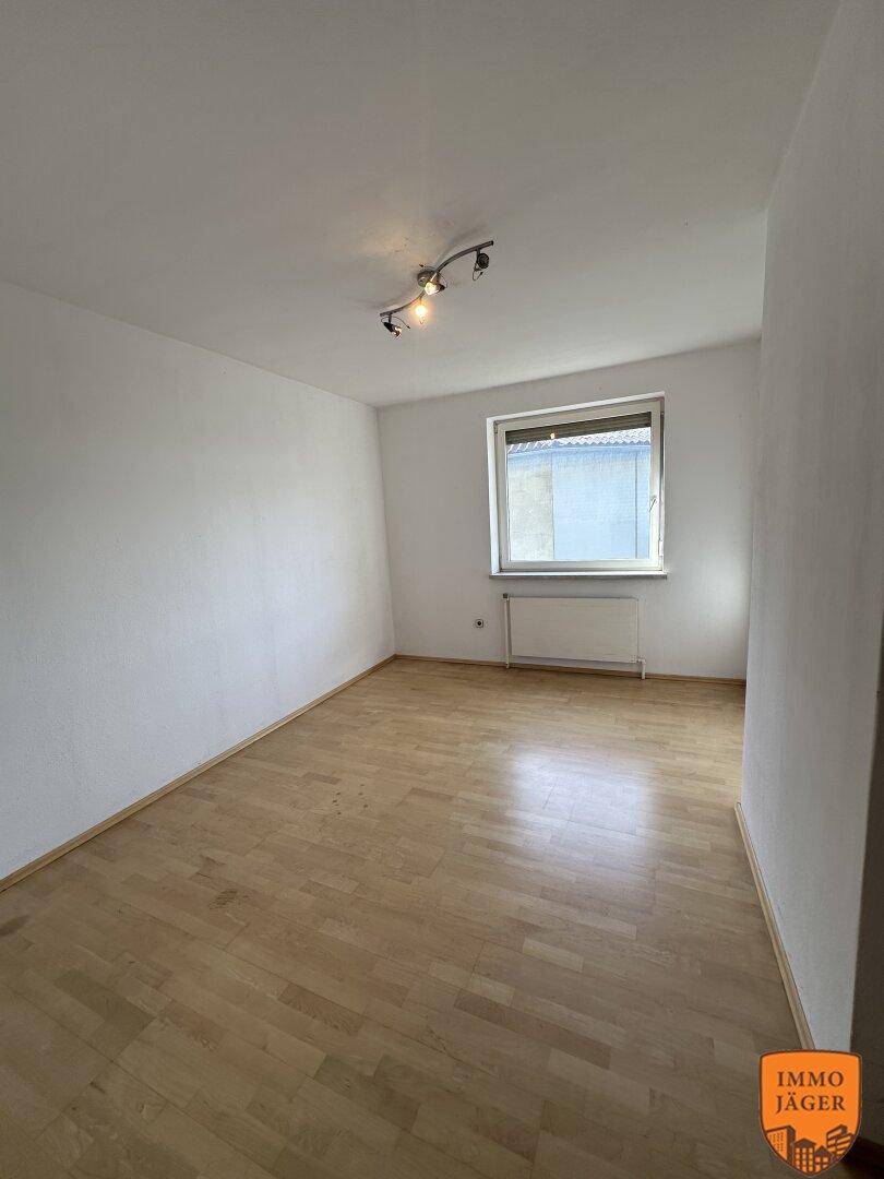 Leeres Schlafzimmer mit Parkettboden und einem Fenster, das ausreichend Tageslicht in den Raum lässt.