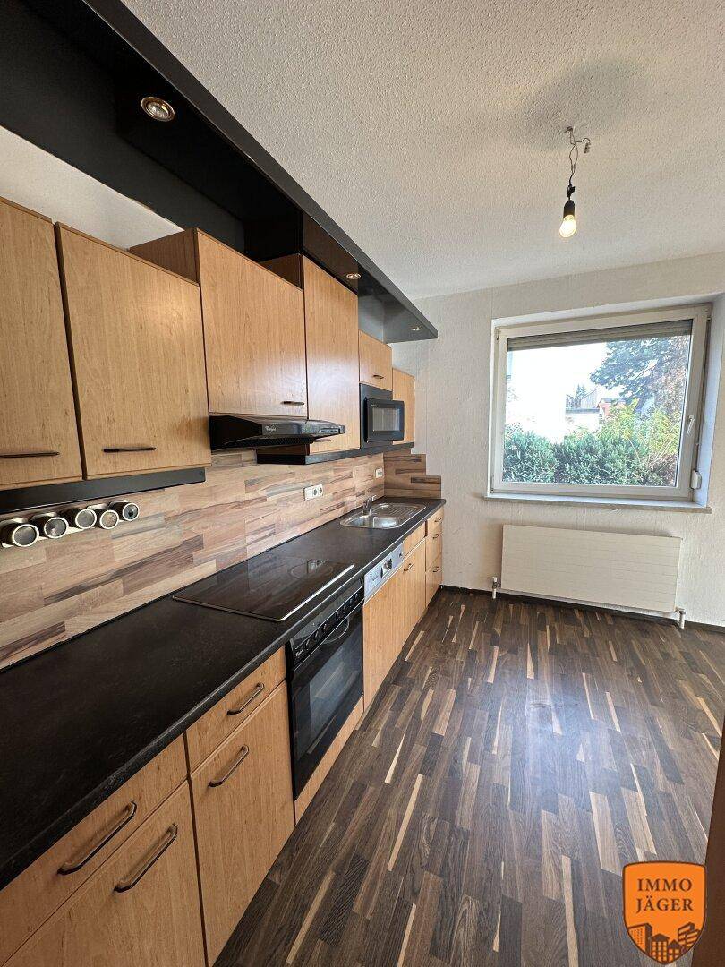 Funktionale Küche mit Holzschränken, dunkler Arbeitsplatte und integrierten Geräten, gut beleuchtet.