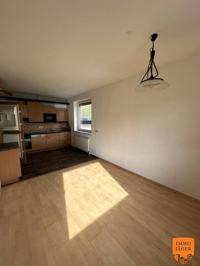 Offener Küchenbereich mit Holzeinbauten und angrenzendem Essbereich, beleuchtet durch ein Fenster.