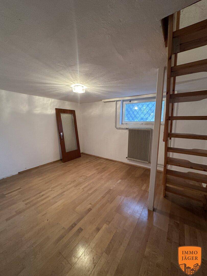 Heller Kellerraum mit Parkettboden, einem Fenster und einer Holztreppe, die in ein höheres Stockwerk führt.