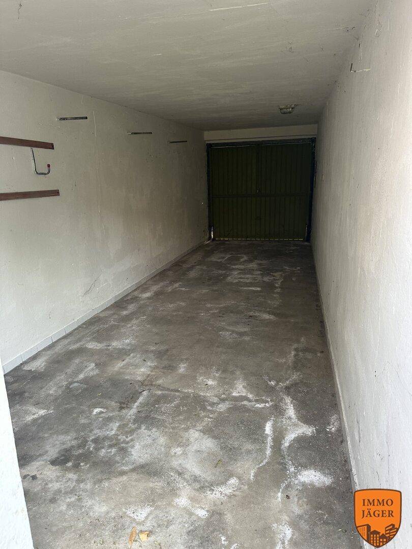 Lange, schmale Garage mit Betonboden und Metalltor, bietet Platz für ein Fahrzeug.