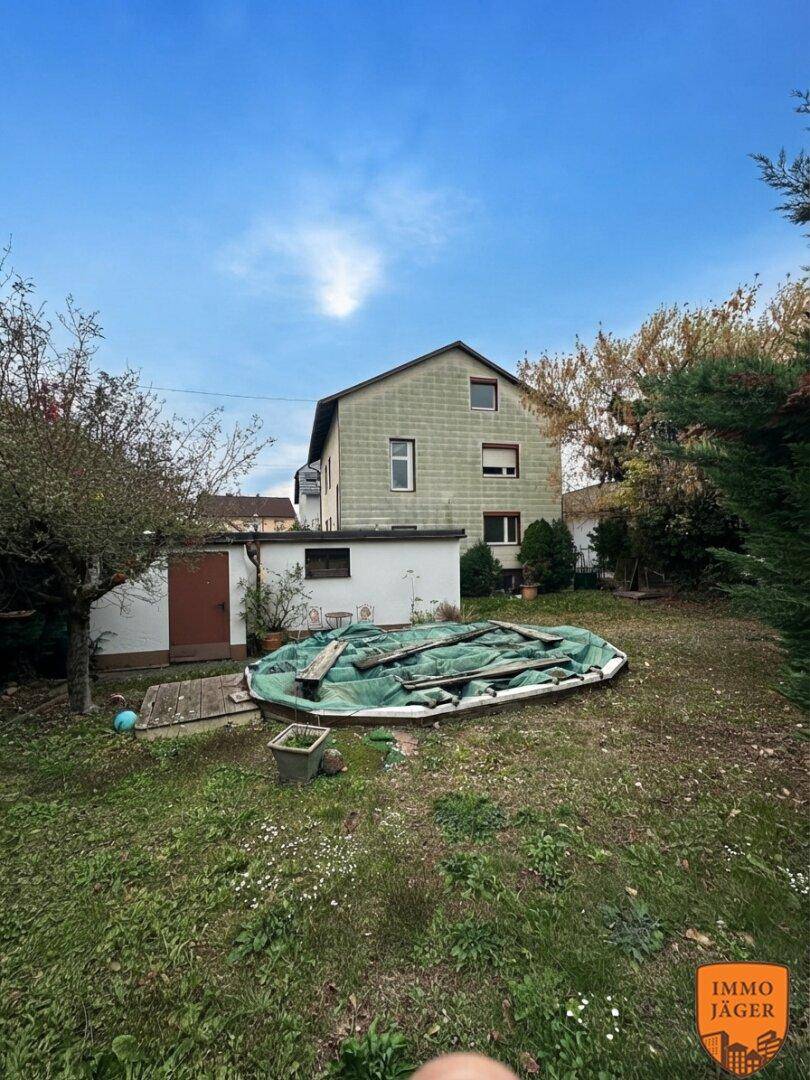 Großer Gartenbereich mit Rasen, Bäumen und einer abgedeckten Pool- oder Teichanlage im Hintergrund.