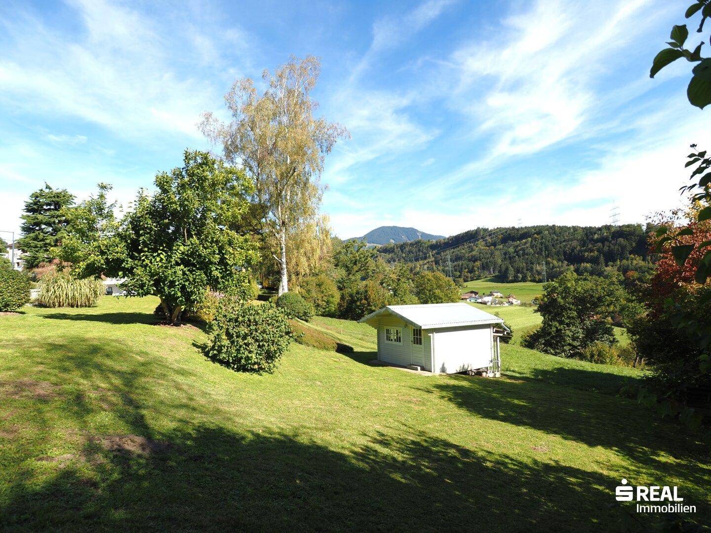 Weitläufige Grünfläche mit einem kleinen Gartenhaus und Blick auf die sanften Hügel in der Ferne.
