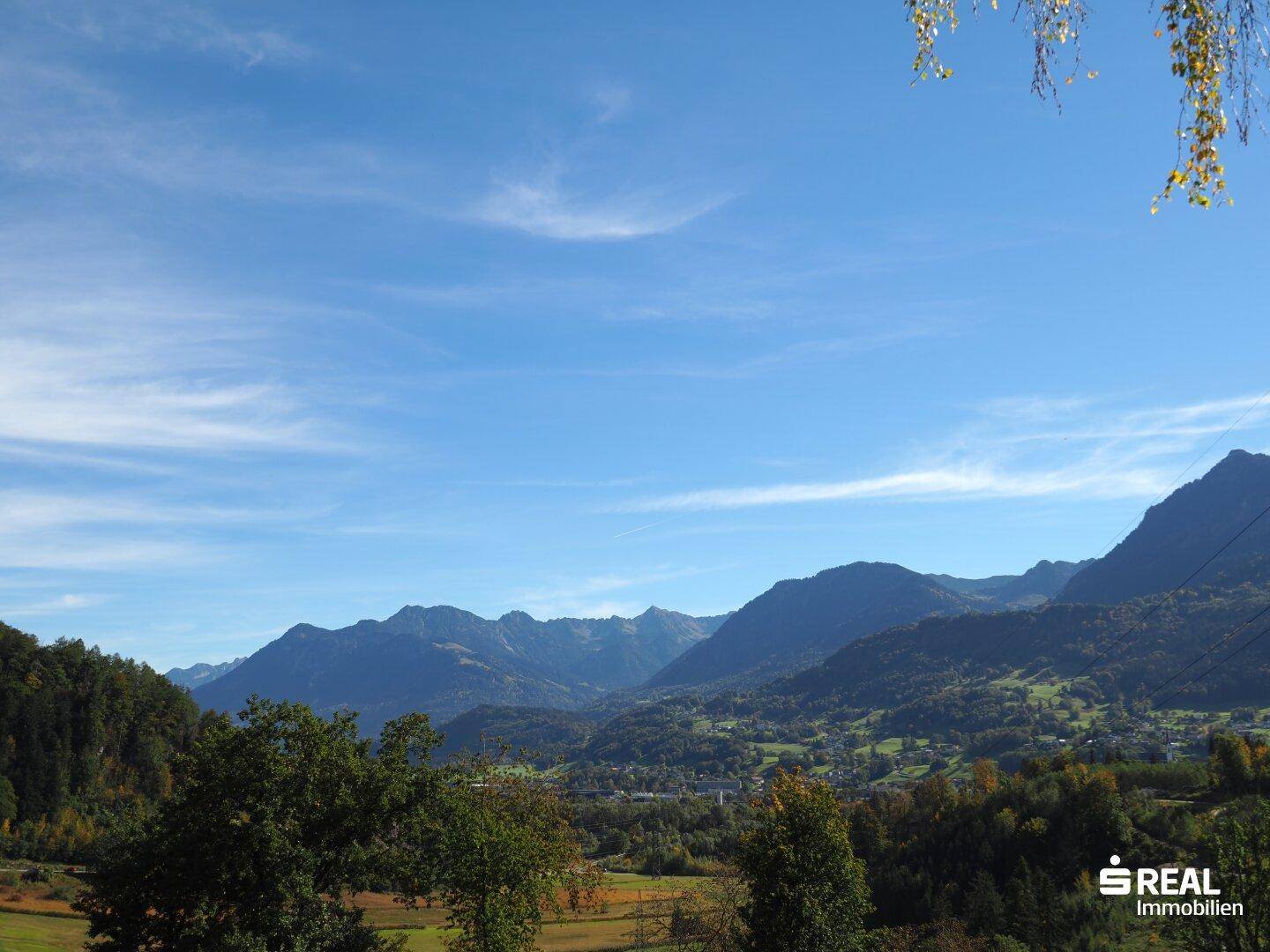 Weitläufiger Panoramablick über die grüne Landschaft und majestätische Berge unter strahlend blauem Himmel.