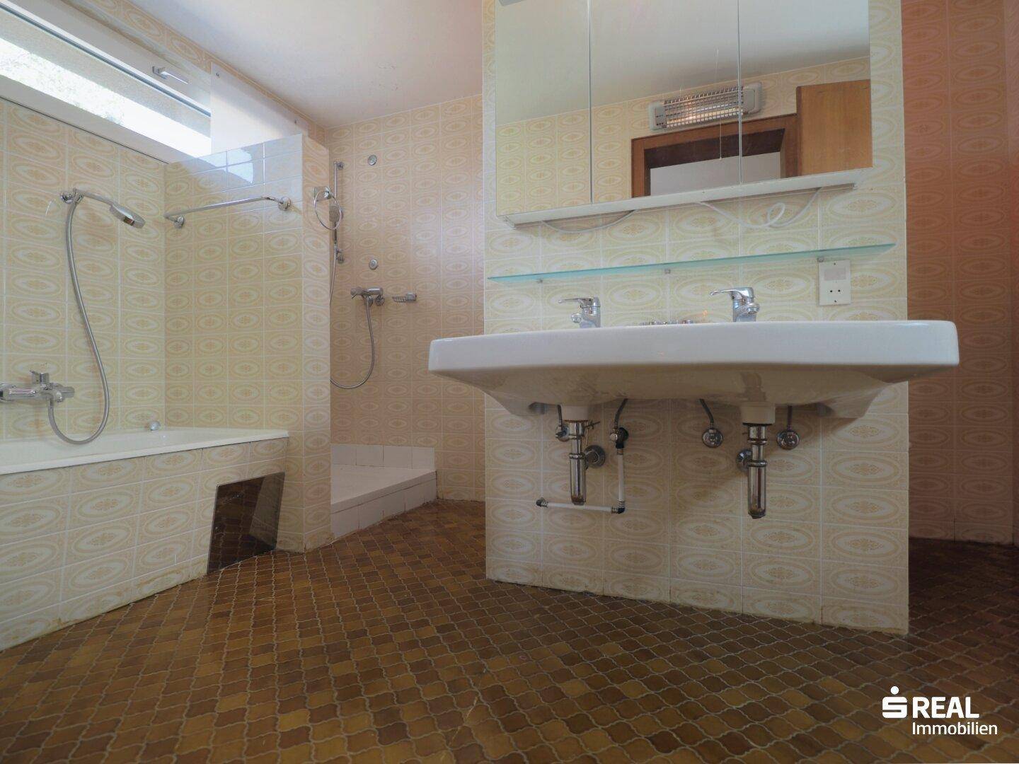 Badezimmer mit Doppelwaschbecken, Badewanne und Duschbereich, gefliest in einem älteren Stil.