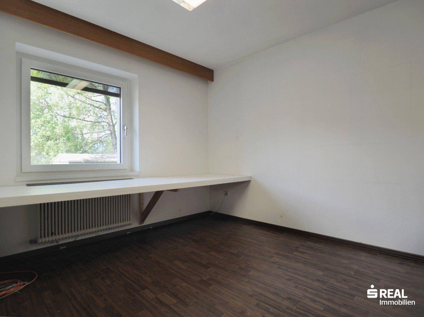 Helles Zimmer mit dunklem Holzboden, Fenster und einer langen Arbeitsplatte unter dem Fenster.