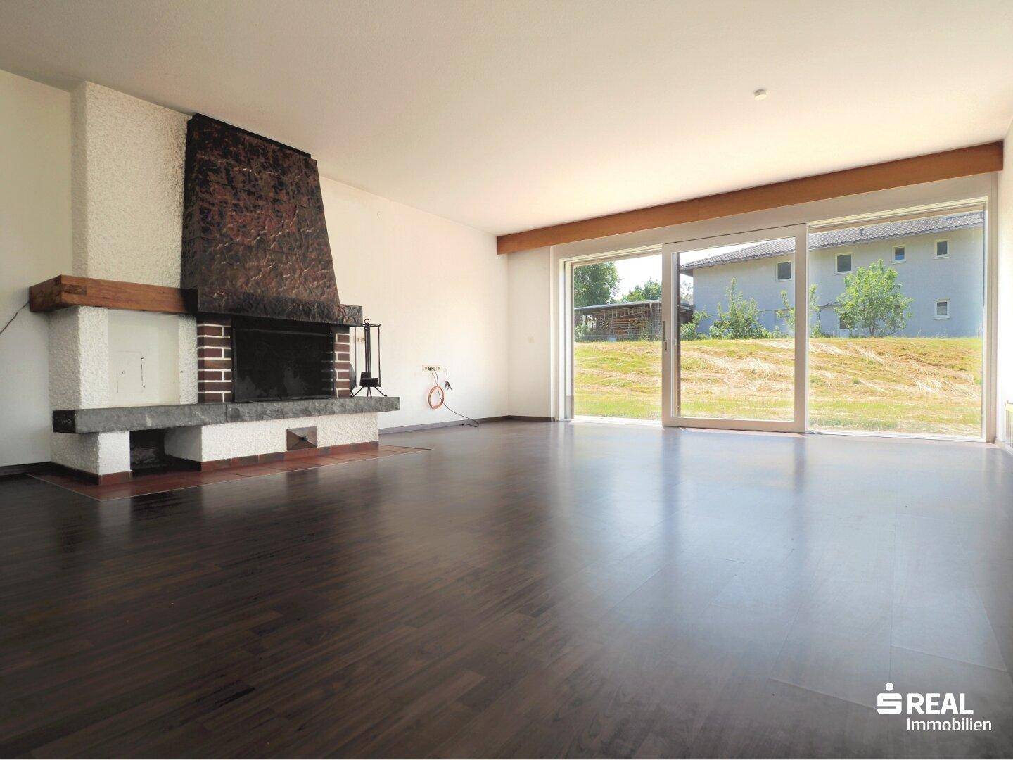 Großzügiges Wohnzimmer mit Kamin, dunklem Holzboden und großen Schiebetüren zum Garten.