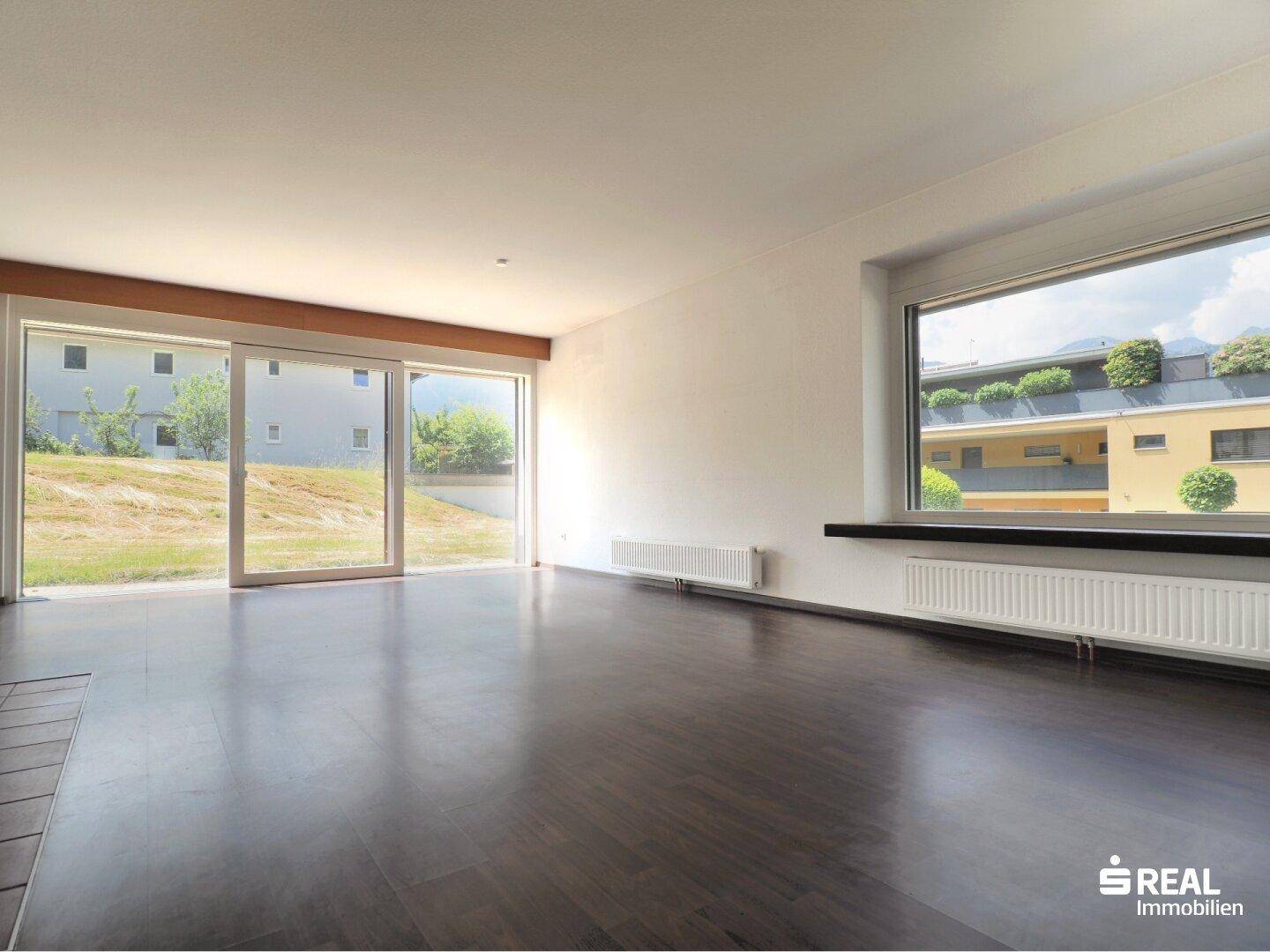 Helles Wohnzimmer mit dunklem Holzboden, großen Fenstern und Zugang zum Gartenbereich.