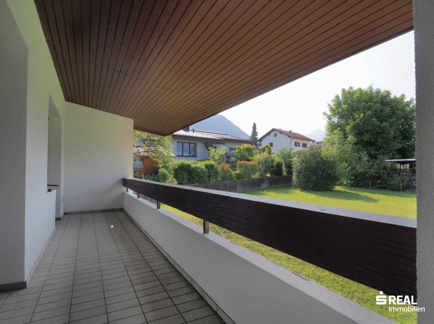 Überdachter Balkon mit Fliesenboden und Blick auf den Garten sowie die umliegende Wohngegend.