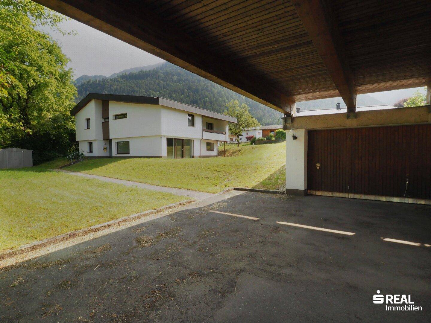 Überdachter Carport und Garage mit Blick auf das Haupthaus und die grüne Umgebung.