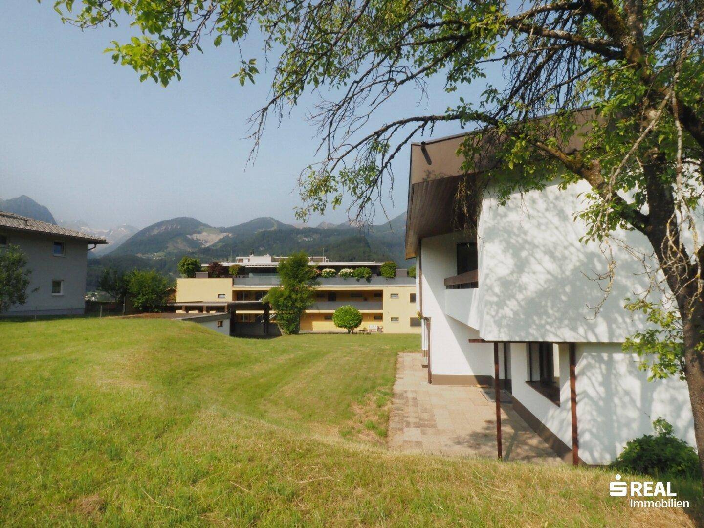Haus mit großer Rasenfläche und Terrasse, umgeben von Natur und mit Bergblick.