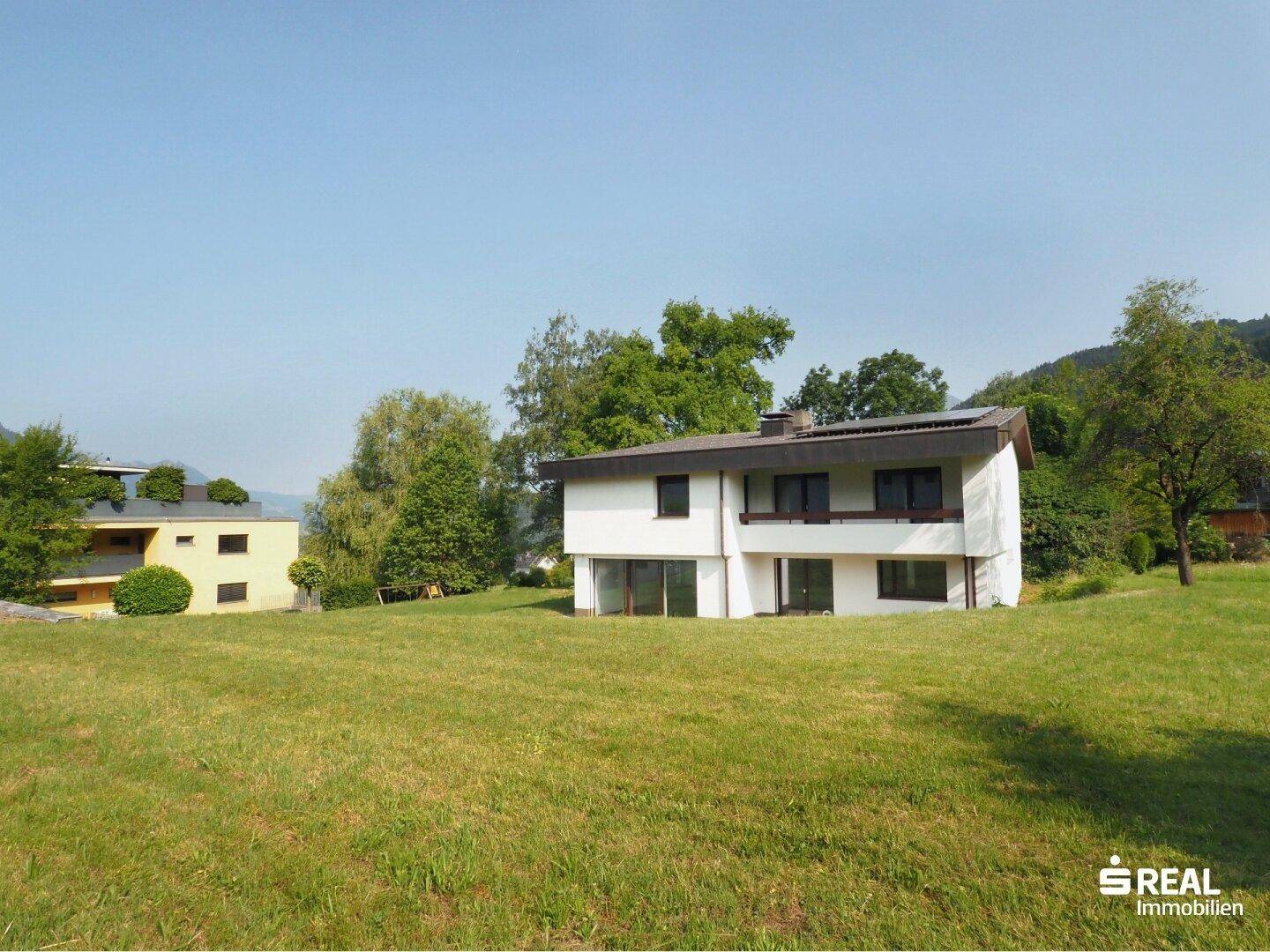 Weißes Einfamilienhaus mit großem, gepflegtem Rasen und Blick auf die umliegende Natur.