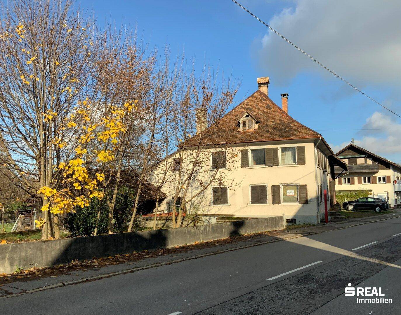 Traditionelles Wohnhaus mit Satteldach und Fensterläden, umgeben von Bäumen im Herbst.