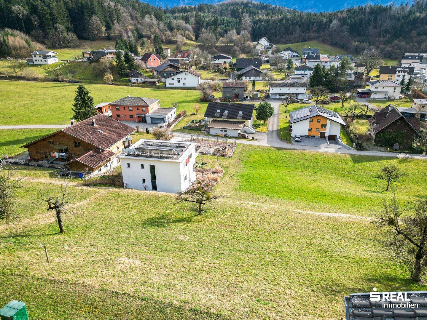 Luftaufnahme einer Wohngegend mit grünen Flächen und einem Gebäude mit Solaranlage auf dem Dach.