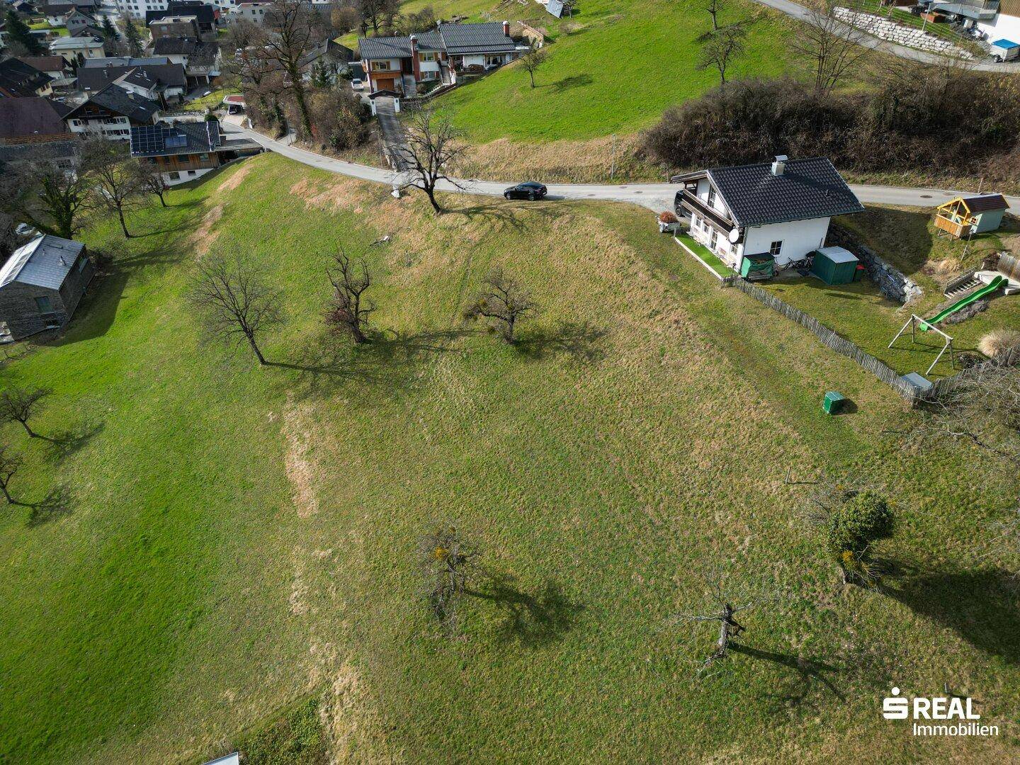 Panoramablick auf ein Wohnhaus auf einem sonnigen Hügel, umgeben von grünen Wiesen und Bergen.