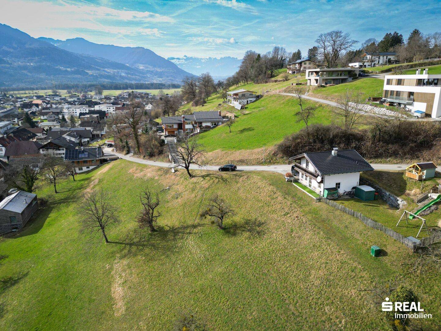 Idyllische Luftansicht eines Hauses auf einem grünen Hügel mit weitem Blick auf die umliegende Bergwelt.