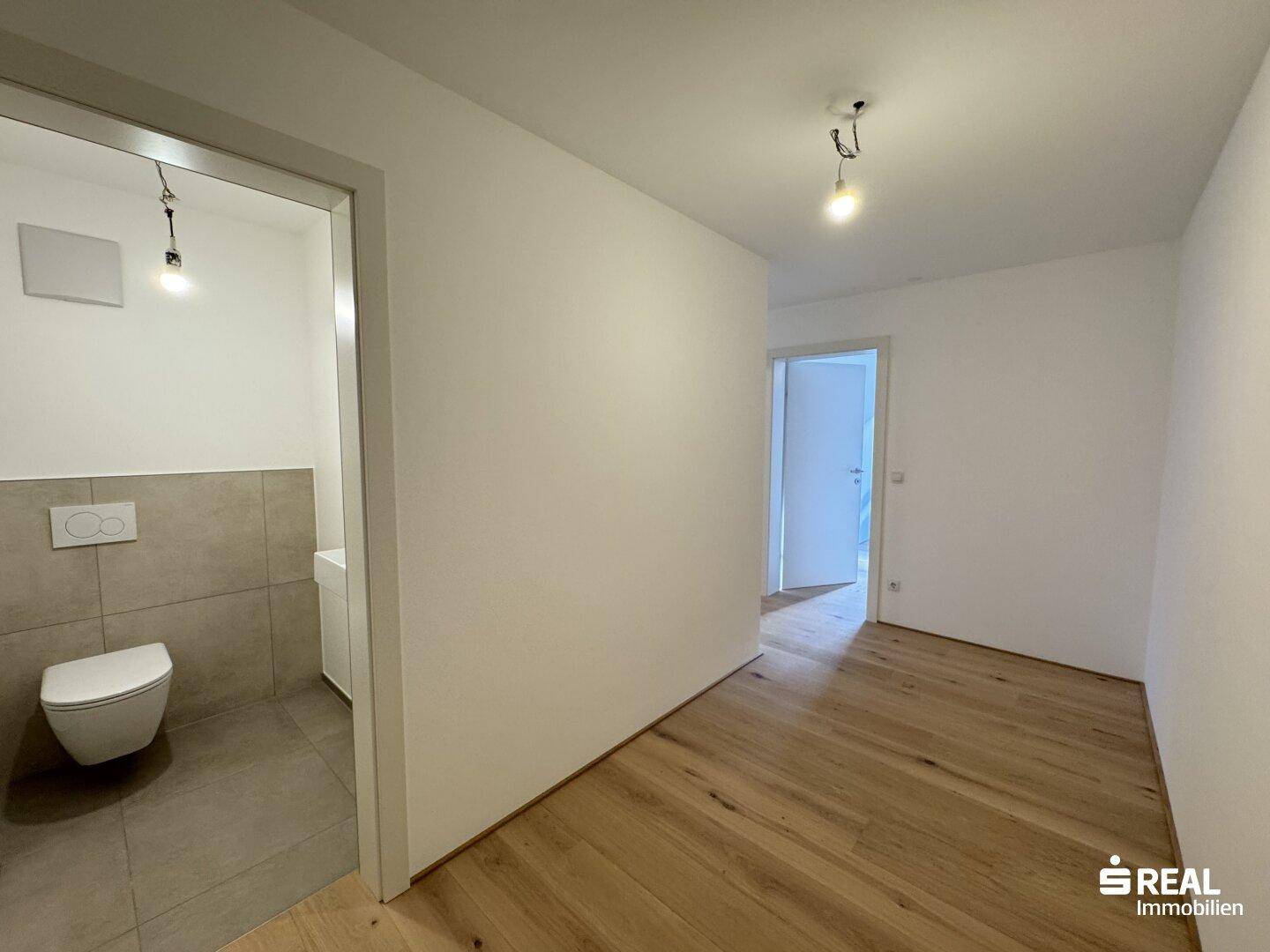 Heller Flur mit Holzparkettboden und Zugang zu einem modernen WC.