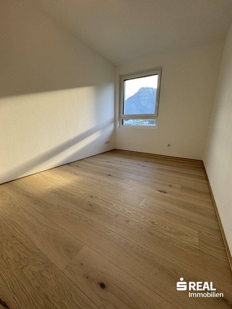 Helles Schlafzimmer mit Holzparkettboden und Fenster mit Bergblick.