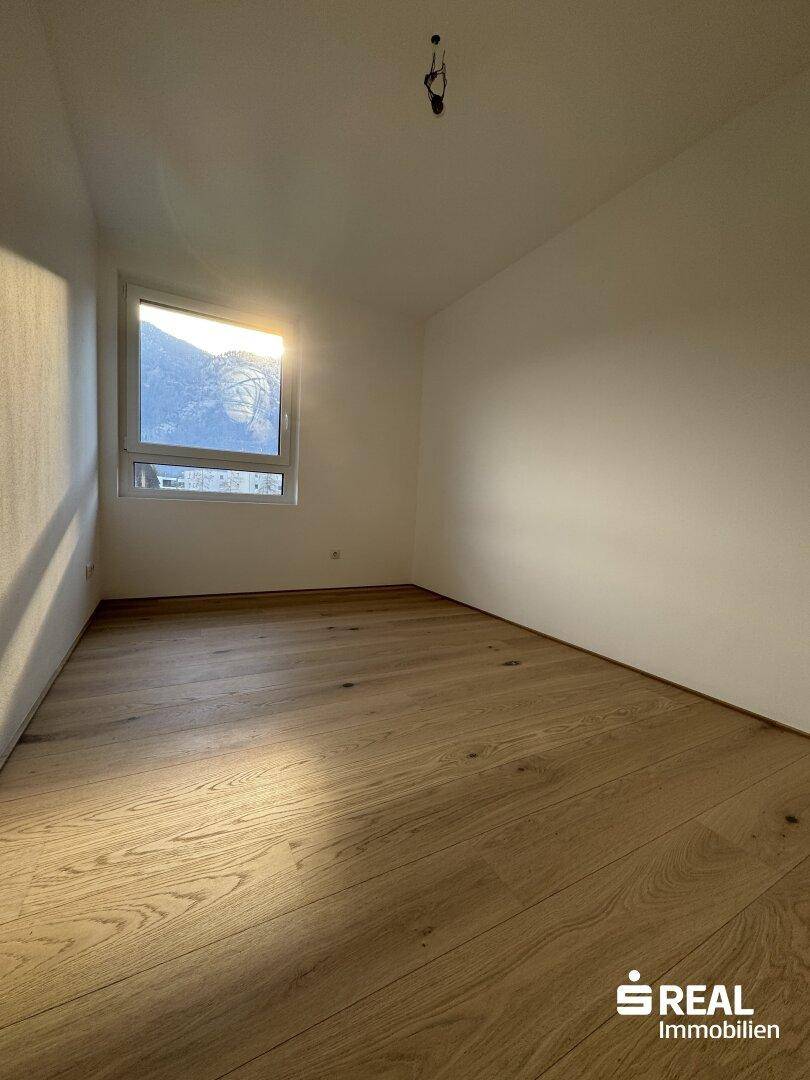 Sonniger Raum mit Holzparkettboden und Fenster, das viel natürliches Licht hereinlässt.