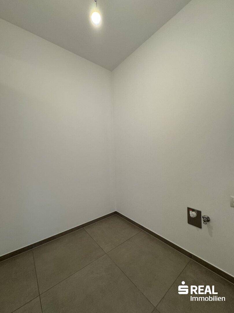 Kleiner Hauswirtschaftsraum mit Fliesenboden und Anschlüssen für Waschmaschine oder Trockner.