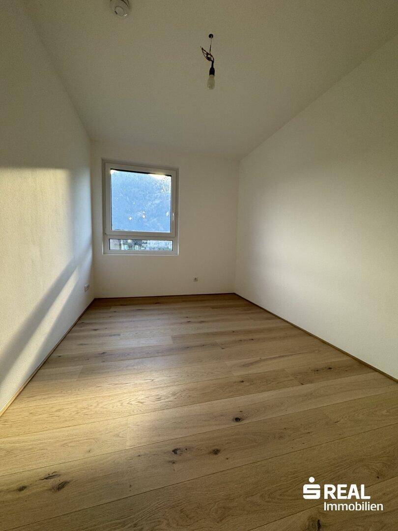 Helles Schlafzimmer mit Holzparkettboden und Fenster, das den Raum gut belichtet.