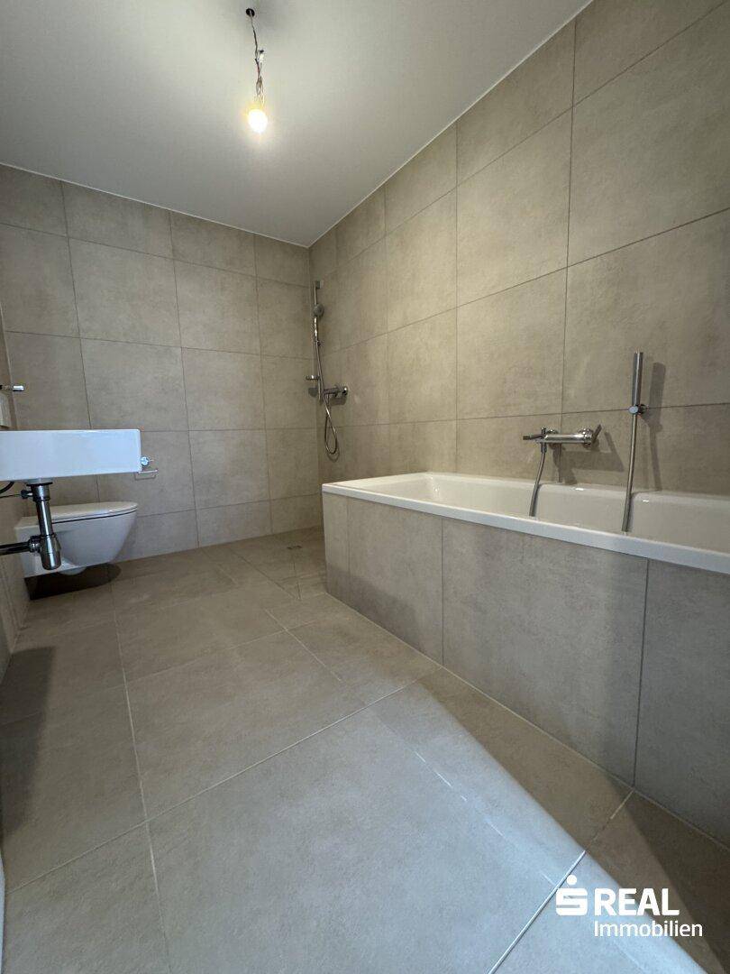 Modernes Badezimmer mit hellen Fliesen, Badewanne und wandhängendem WC.