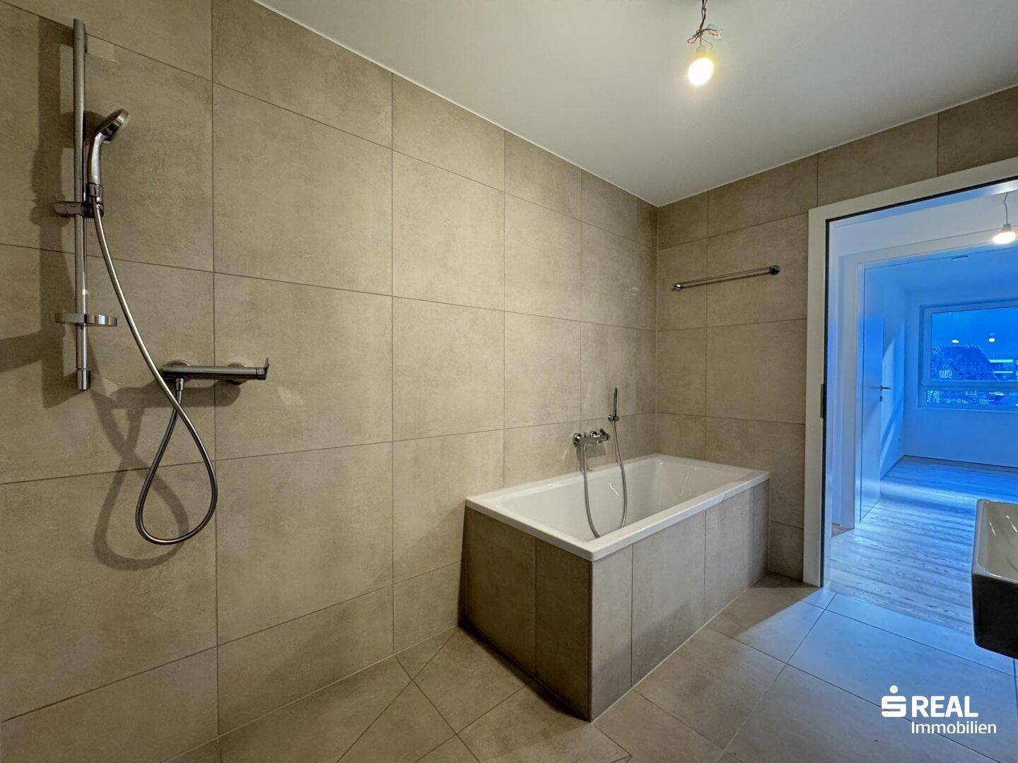 Modernes Badezimmer mit Badewanne, Duscharmatur und hellen Fliesen.
