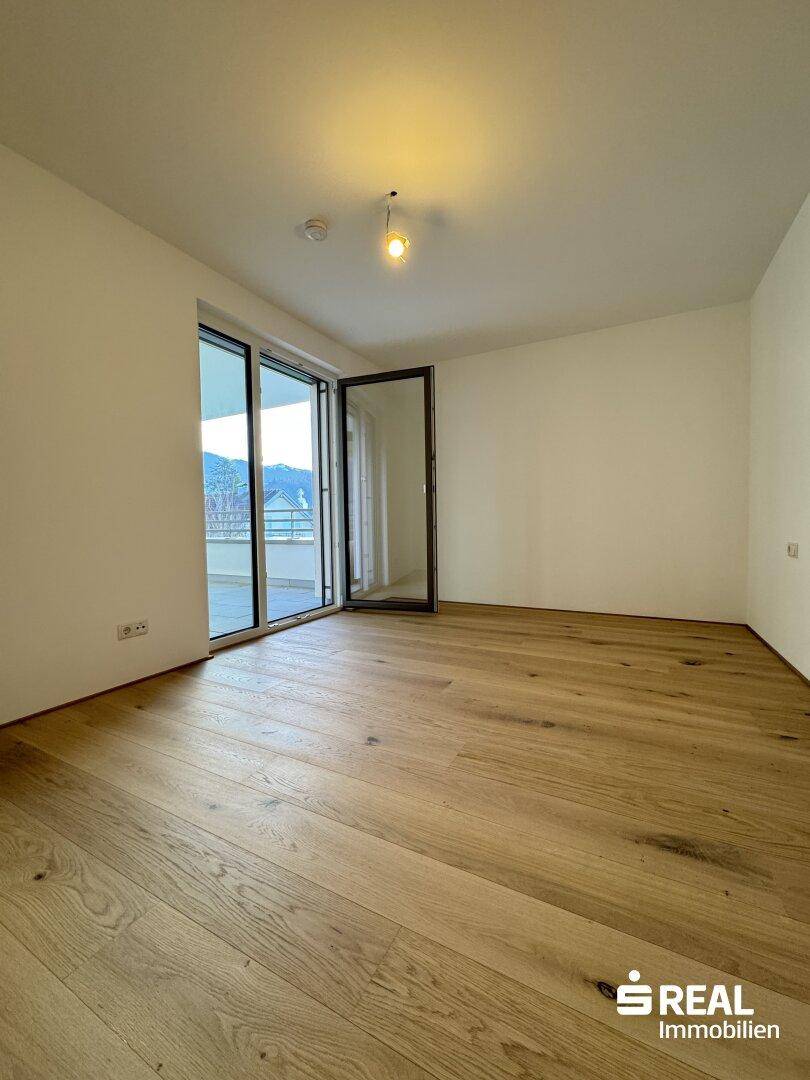 Heller Wohnraum mit Holzparkettboden und direktem Zugang zum Balkon.