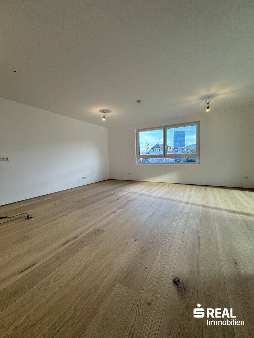 Geräumiger Wohnbereich mit Holzparkettboden und großem Fenster mit Blick auf die Umgebung.