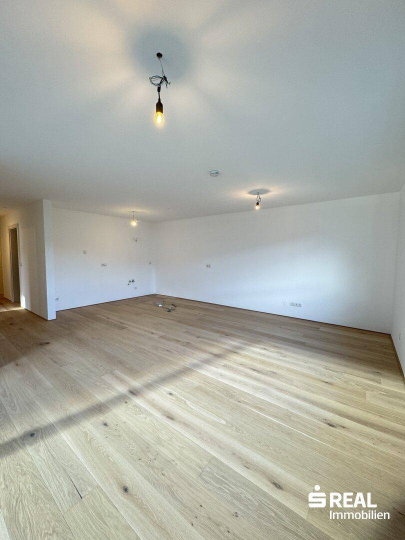 Heller, leerer Wohnbereich mit neuem Holzparkettboden und weißen Wänden.