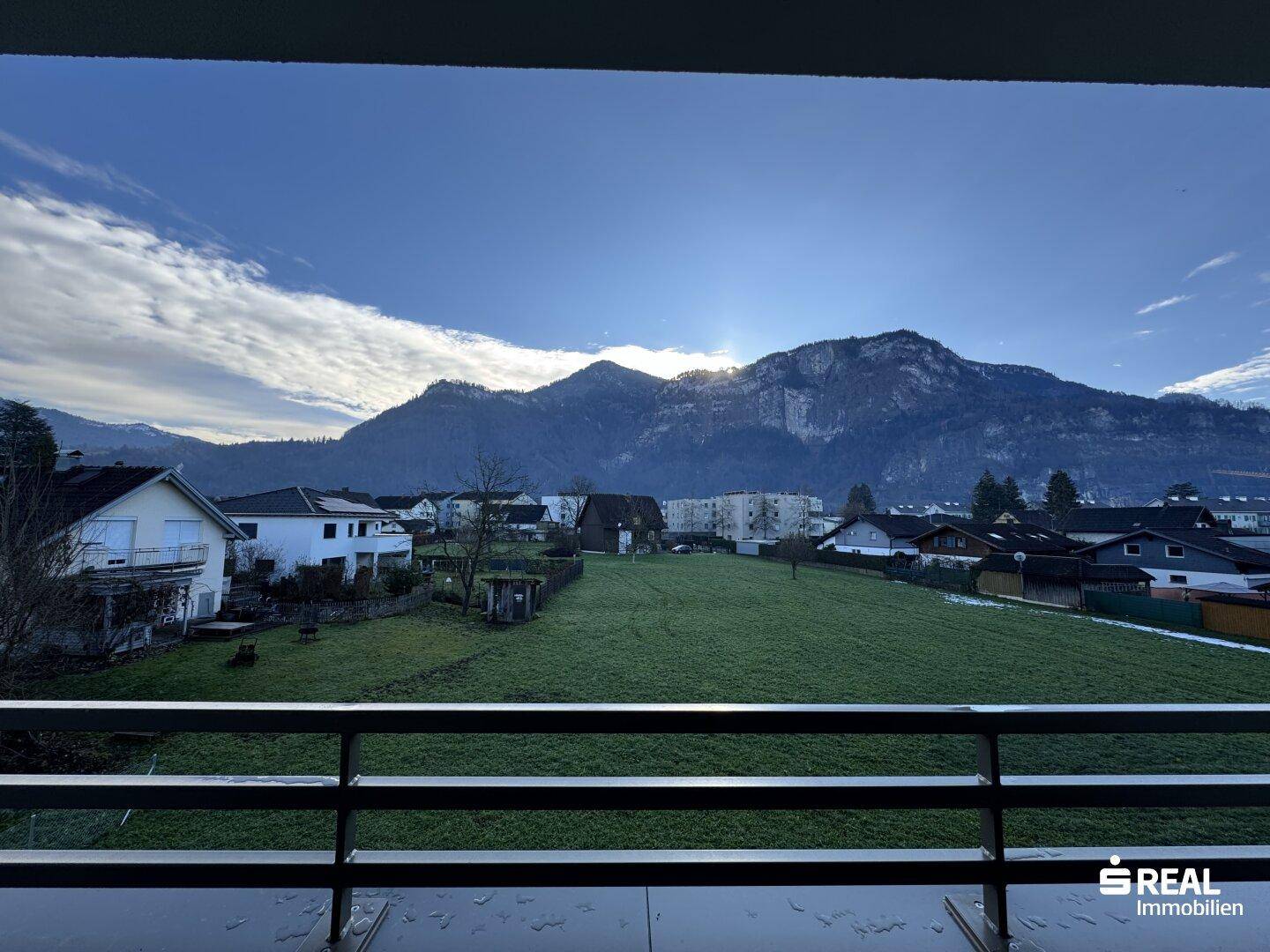 Weitläufiger Blick auf die umliegende Berglandschaft und grüne Felder von einem Balkon aus.