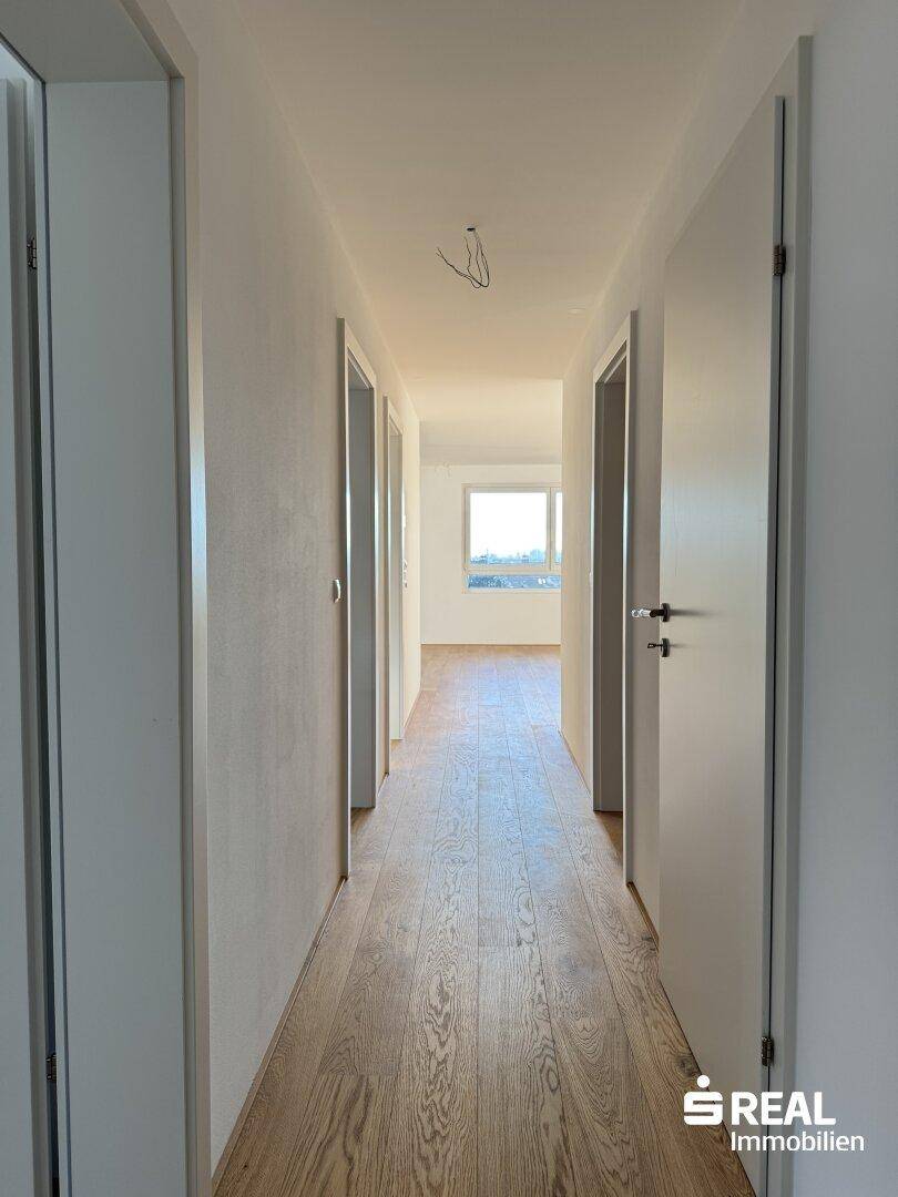 Heller Flur mit Holzboden und mehreren Türen, der zu weiteren Räumen führt.