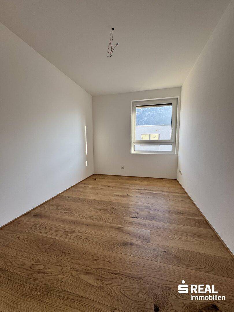 Helles Schlafzimmer mit Holzboden, weißen Wänden und Blick auf die umliegenden Gebäude.