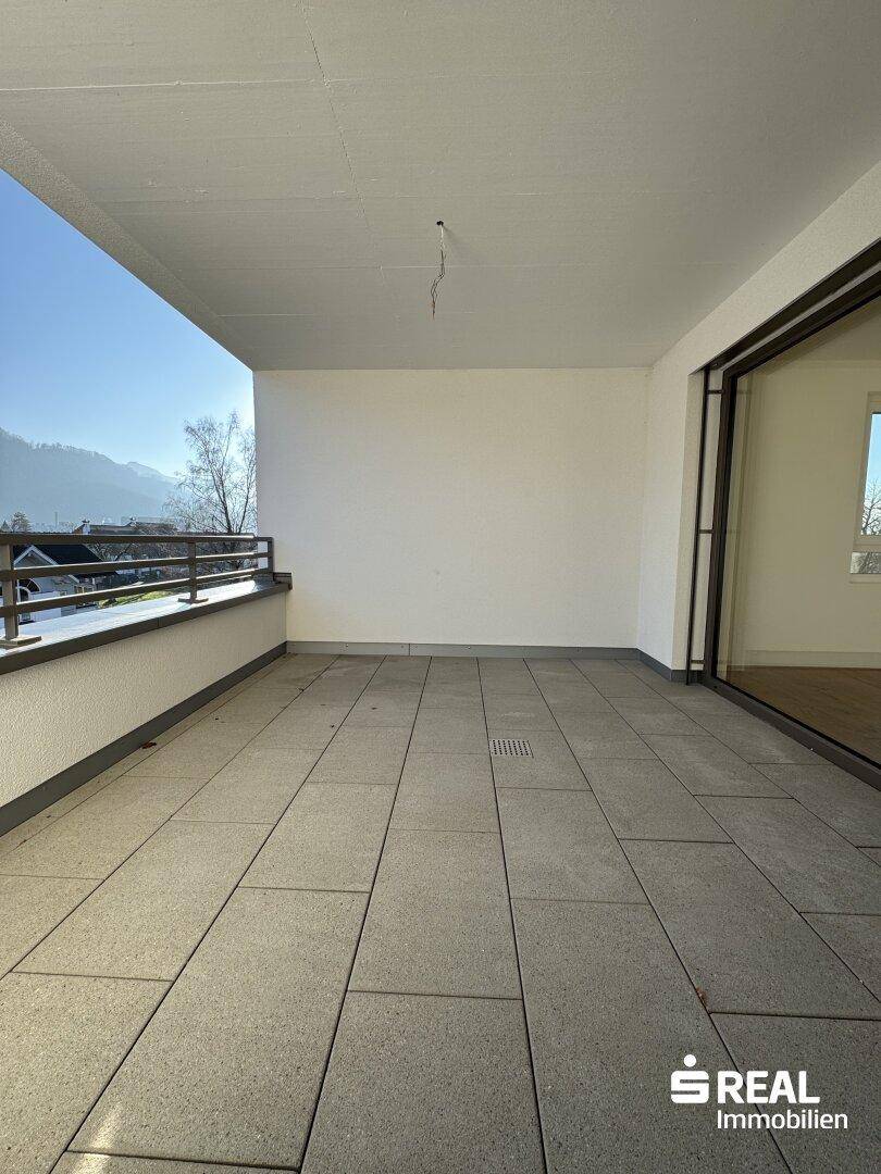 Geräumiger Balkon mit Fliesenboden, Bergblick und Zugang zum Innenbereich durch eine Glasschiebetür.