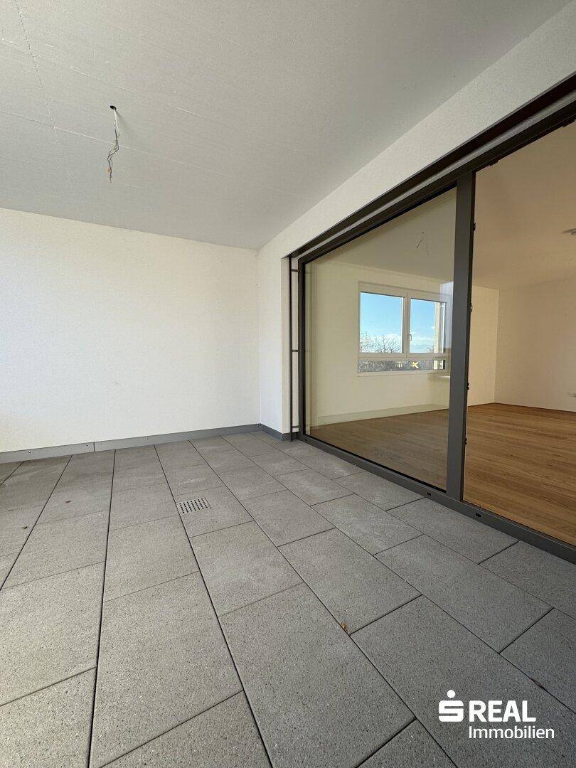 Breiter Balkon mit Fliesenboden und großer Glasschiebetür, die viel Licht in den Wohnraum lässt.